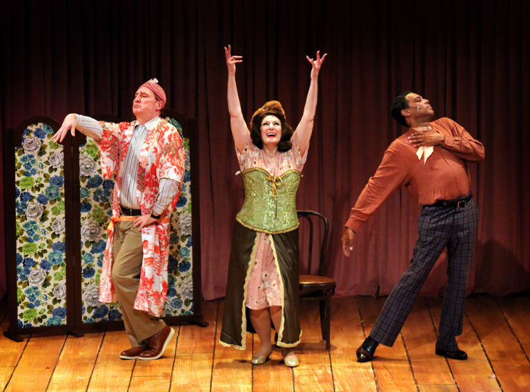 Three adults triumphantly pose—man in dressing gown and turban, woman in corset and fur hat, man in slacks and button down