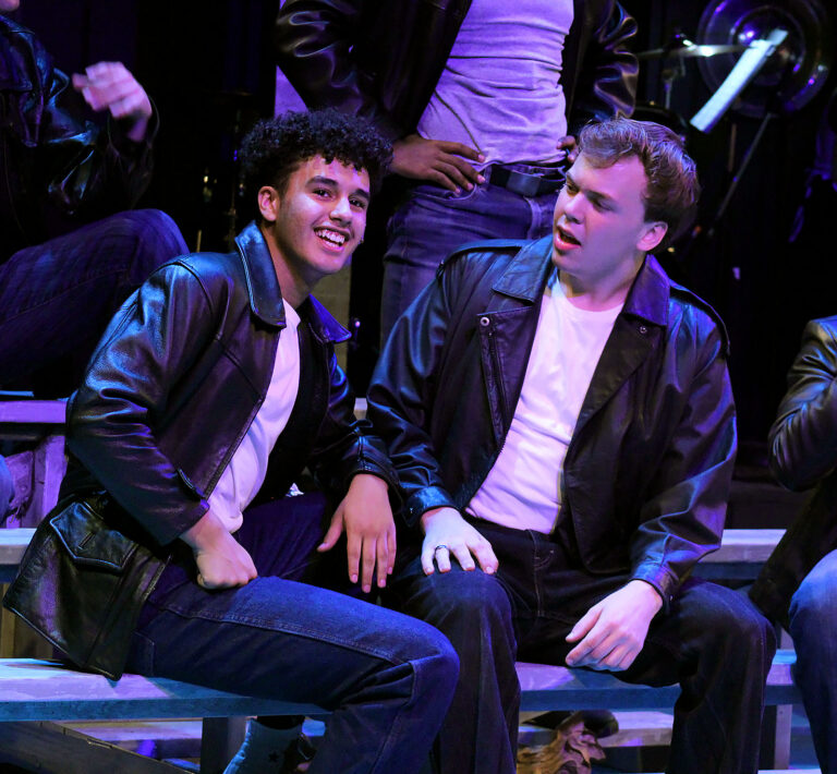 two young men dressed as 1950s greasers sit on bleachers