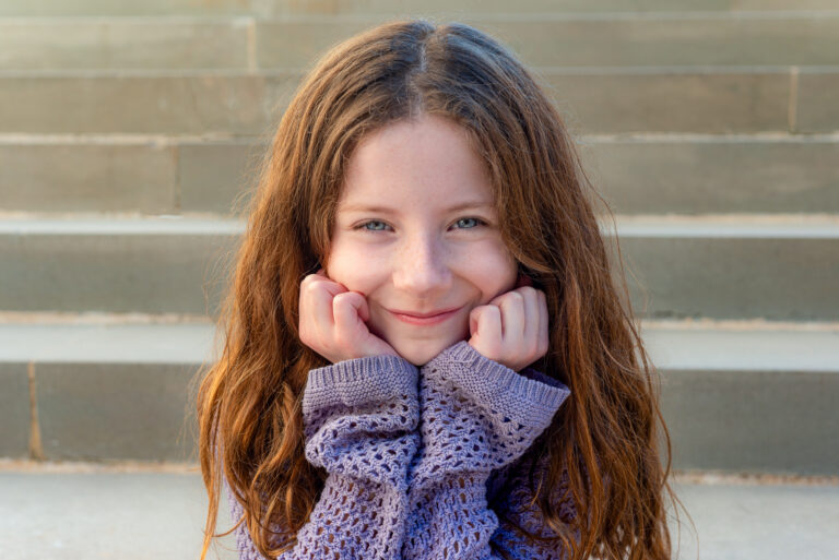young girl sits outside in front of stone steps resting head in hands