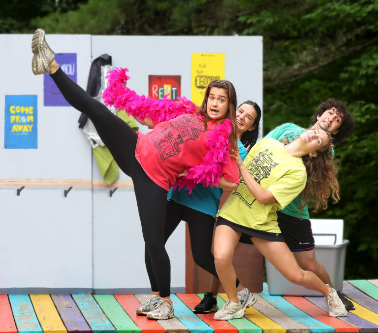 one woman leans back in a high kick while two women and one man hold her up